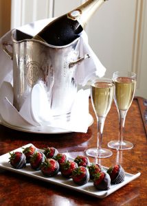 chillled wine bucket with two glasses of white wine beside it and a plate of chocolate covered strawberries