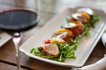 plate of food on wooden table next to glass of red wine